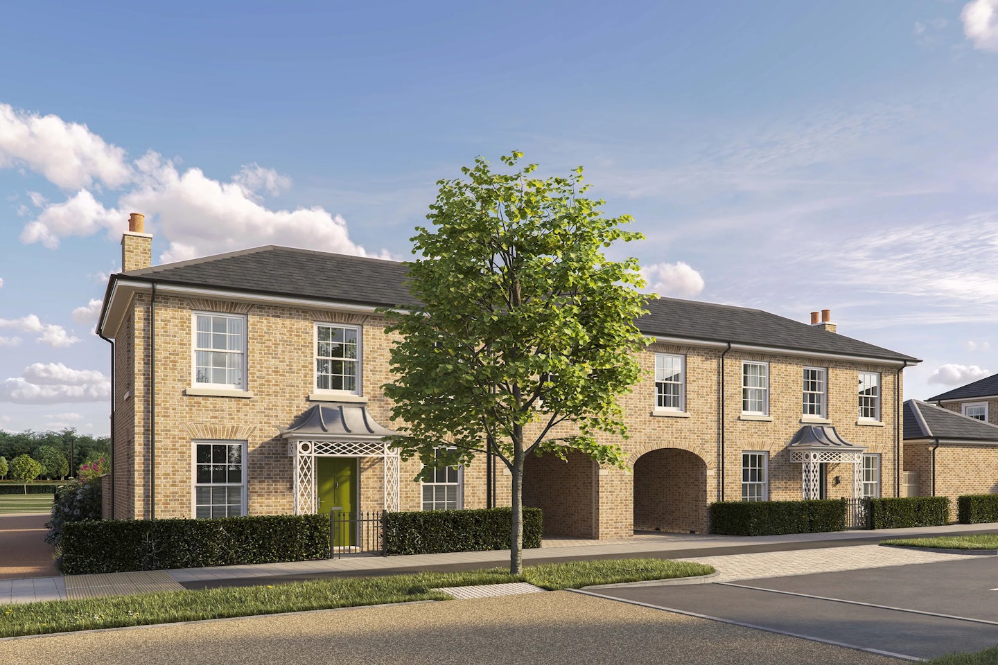 Two-story semi-detached brick houses with pitched roofs and white-framed sash windows. Each house has a front door with a decorative canopy, one painted green and the other partially visible on the right. The property includes two large arched carport openings in the center. A low hedge runs along the front, and a tree is planted on the pavement in the foreground. The sky is bright blue with scattered clouds.