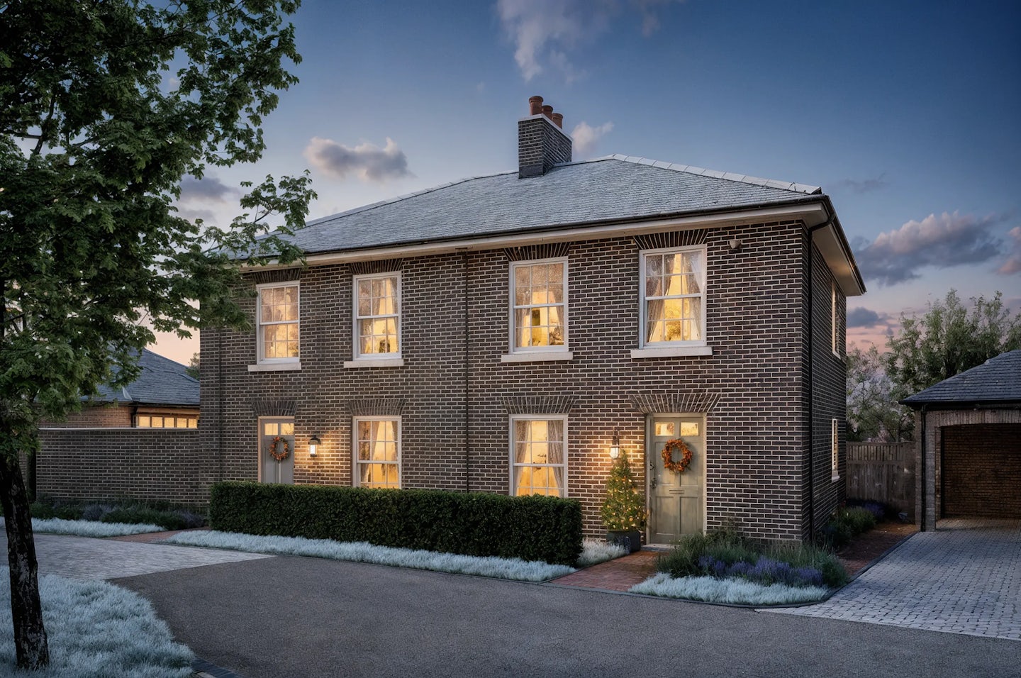 Two-story brick semi-detached house decorated for Christmas with warm white lights around the doorway, a wreath on the door, and a small illuminated tree in the front garden. The photo is taken at dusk with interior lights glowing through sash windows.