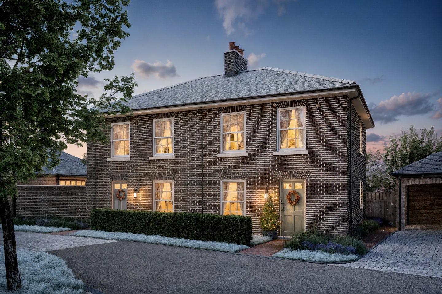 Two-story brick semi-detached house decorated for Christmas with warm white lights around the doorway, a wreath on the door, and a small illuminated tree in the front garden. The photo is taken at dusk with interior lights glowing through sash windows.