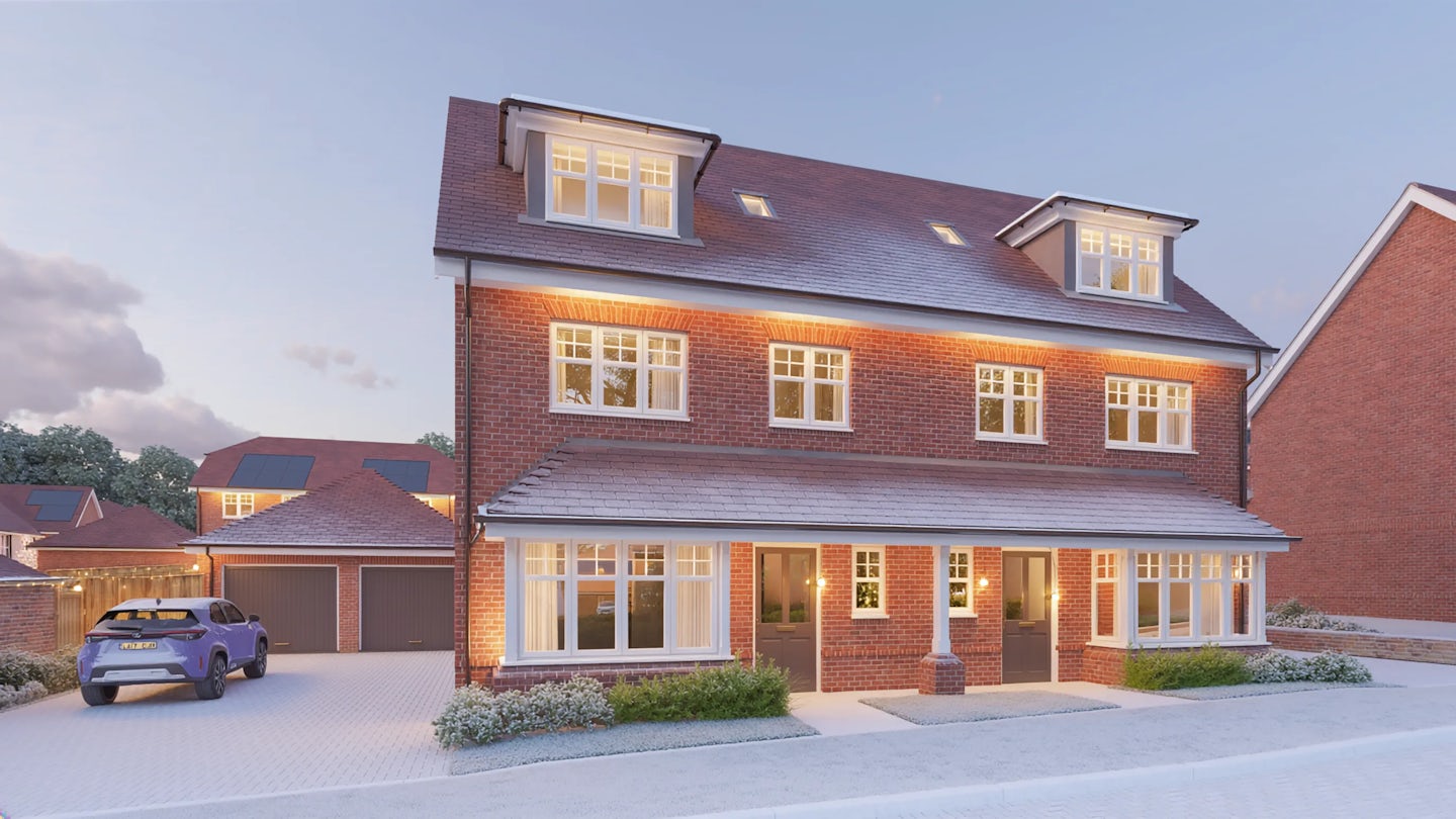 Three-story red-brick townhouse with dormer windows on the top floor, decorated for Christmas with warm white lights along the roofline and around the porch. The property has large sash windows, a paved driveway with a parked car, and landscaped shrubs in front, photographed at dusk.