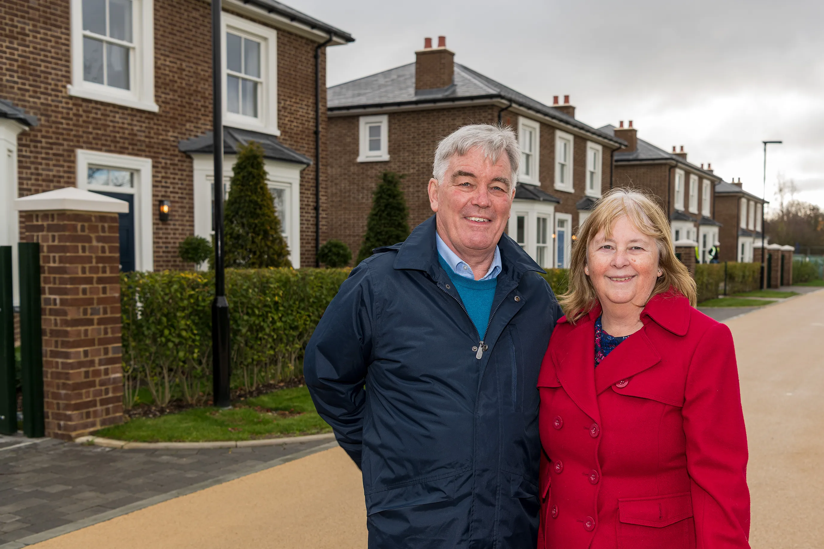 A couple posing on a quiet residential street lined with newly built brick houses.
