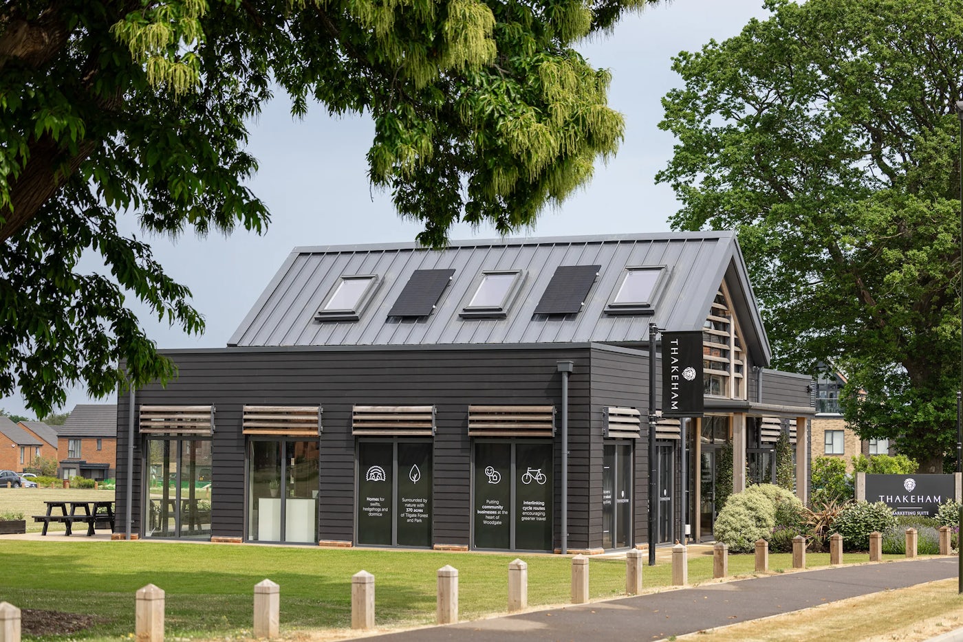 A contemporary community building with dark cladding, large windows, solar panels on the roof, and a green lawn in front.