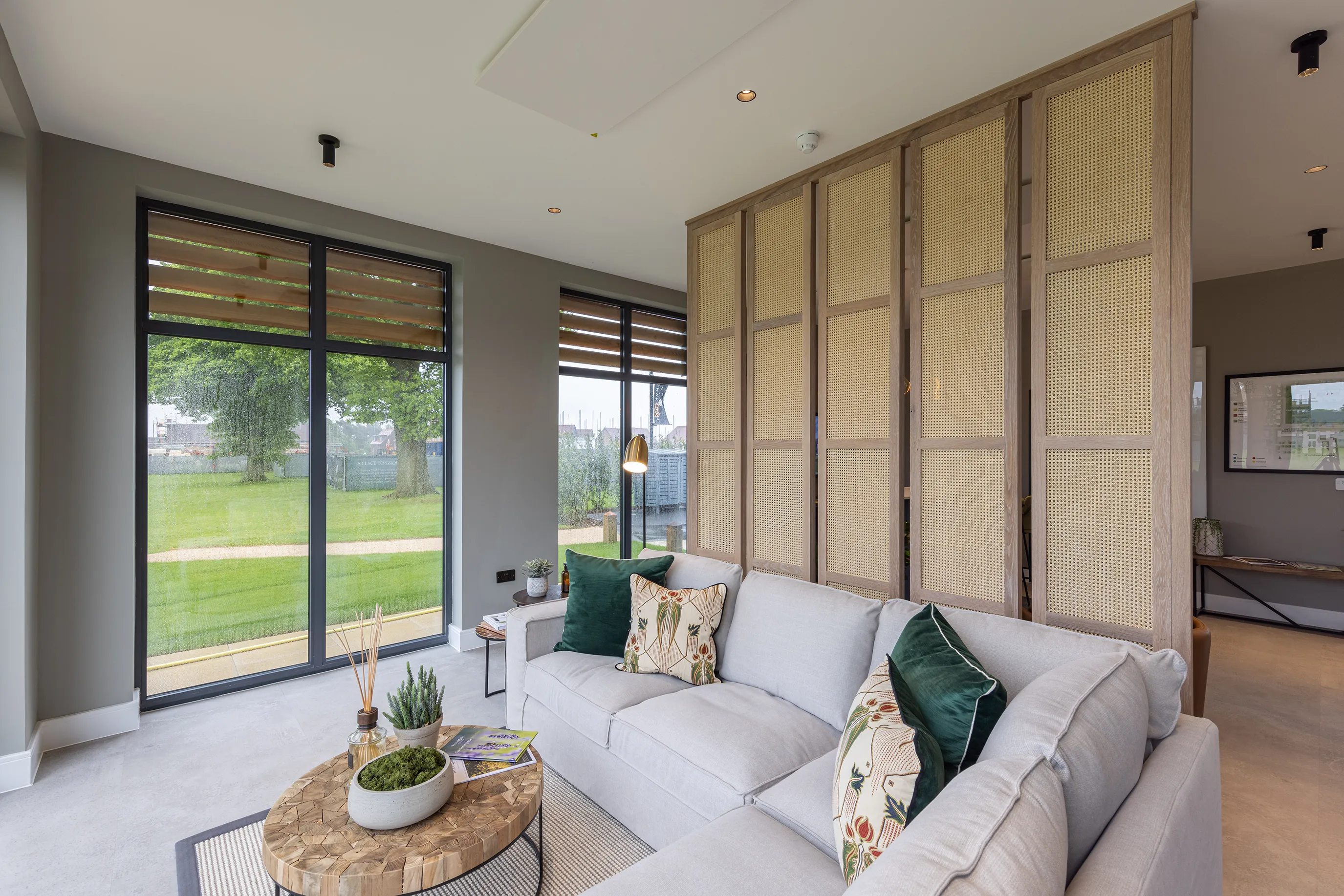 A modern living space with a light sofa, green cushions, a round wooden coffee table, and large glass doors looking out onto a grassy area.