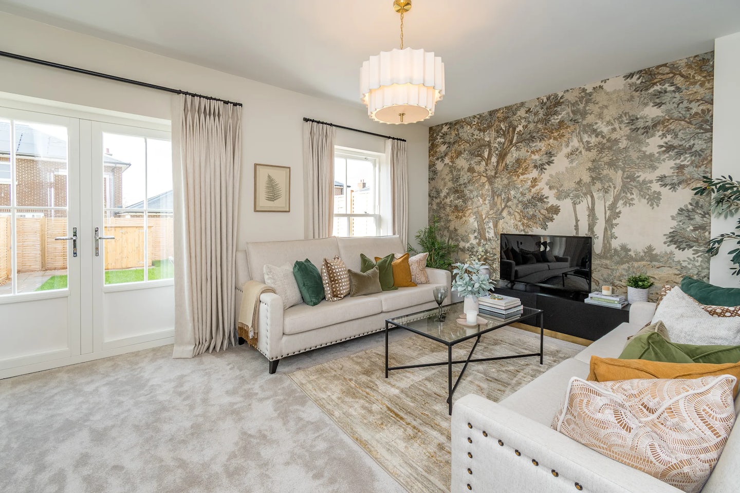 A bright living room with two sofas, a coffee table, patterned feature wallpaper, and glass doors opening to the garden.