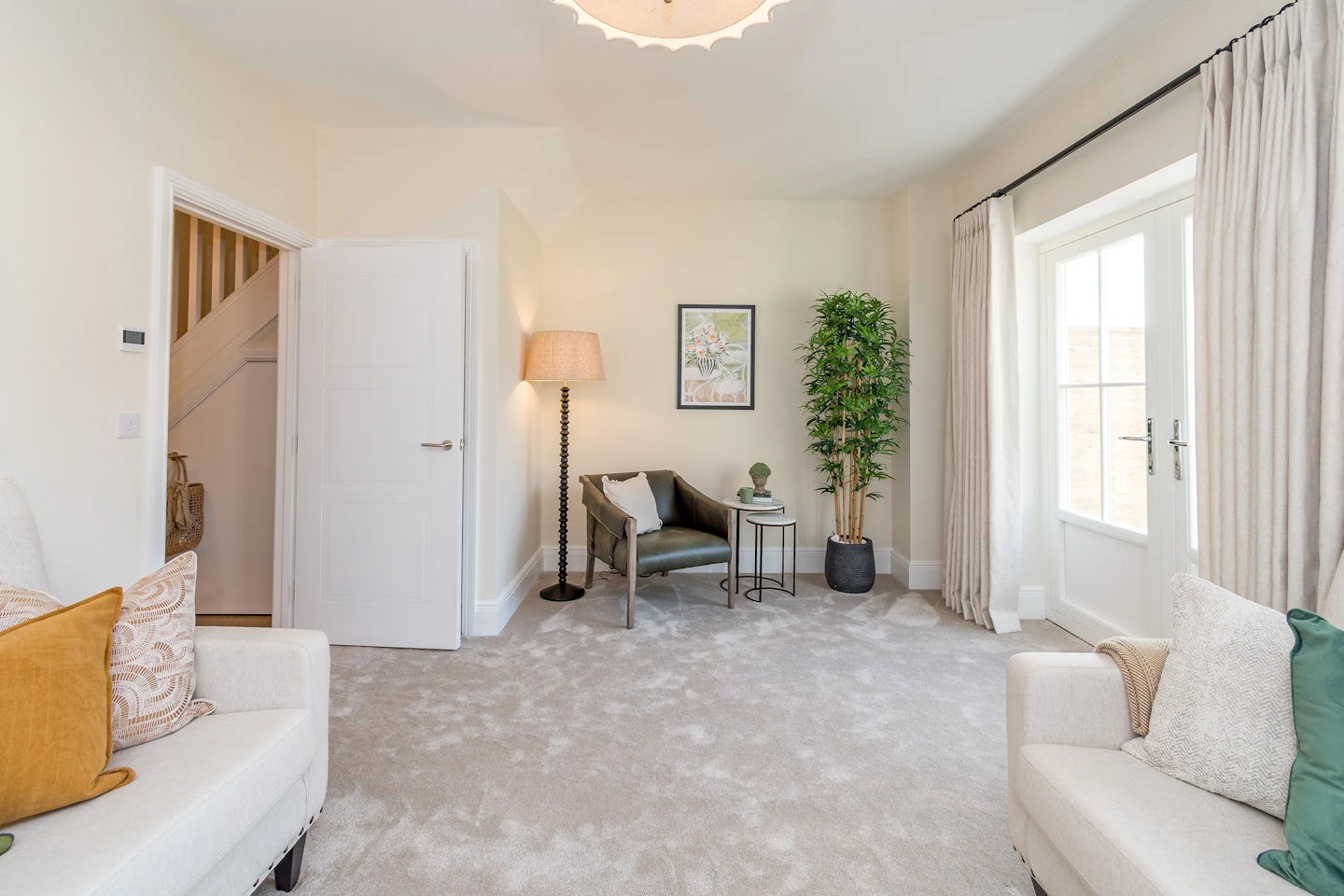 A bright living room with two sofas, a carpeted floor, a chair with a side table, and glass doors opening outside.