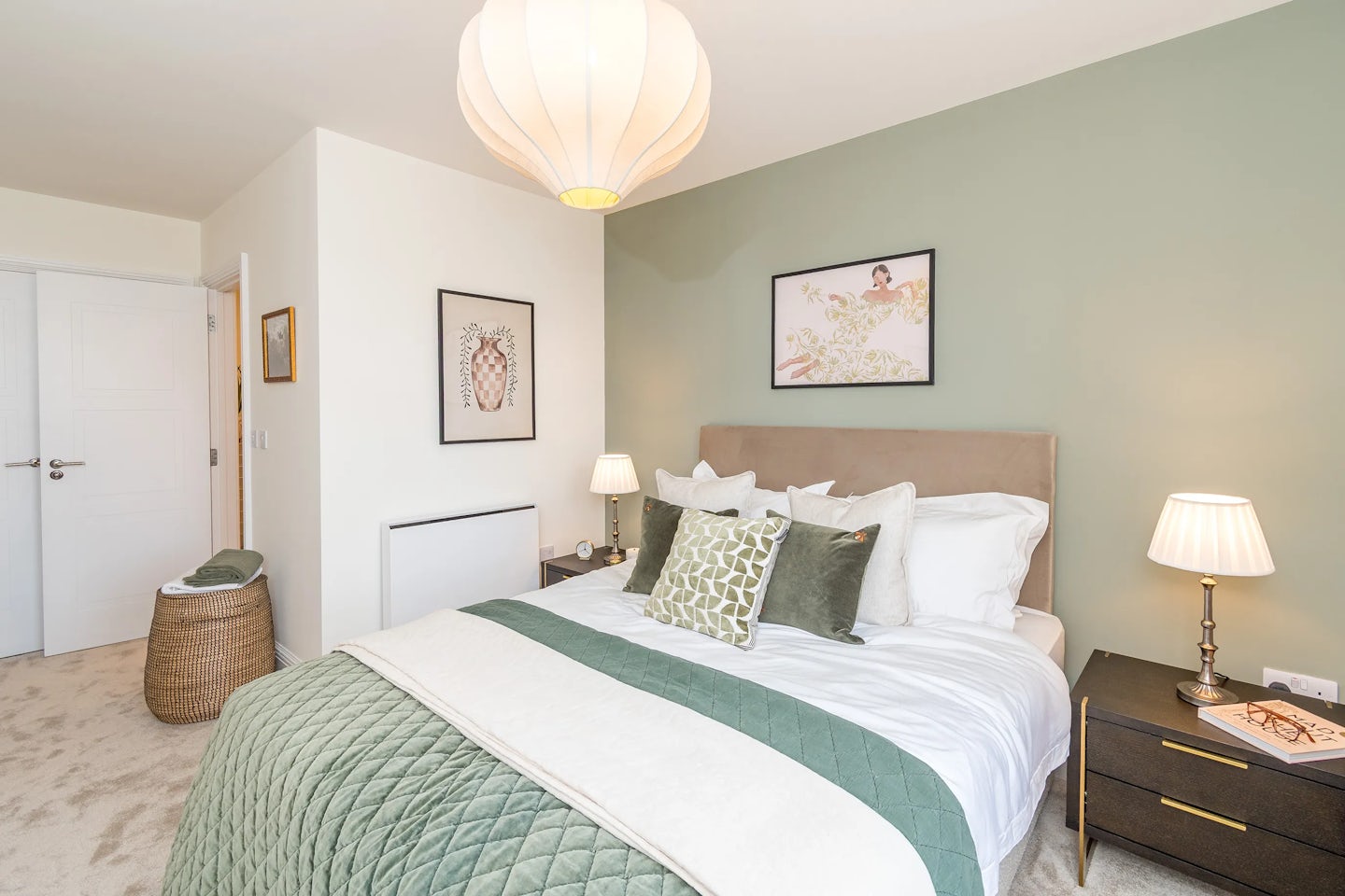 A double bedroom with a neatly made bed, green accent wall, bedside lamps, and framed artwork.