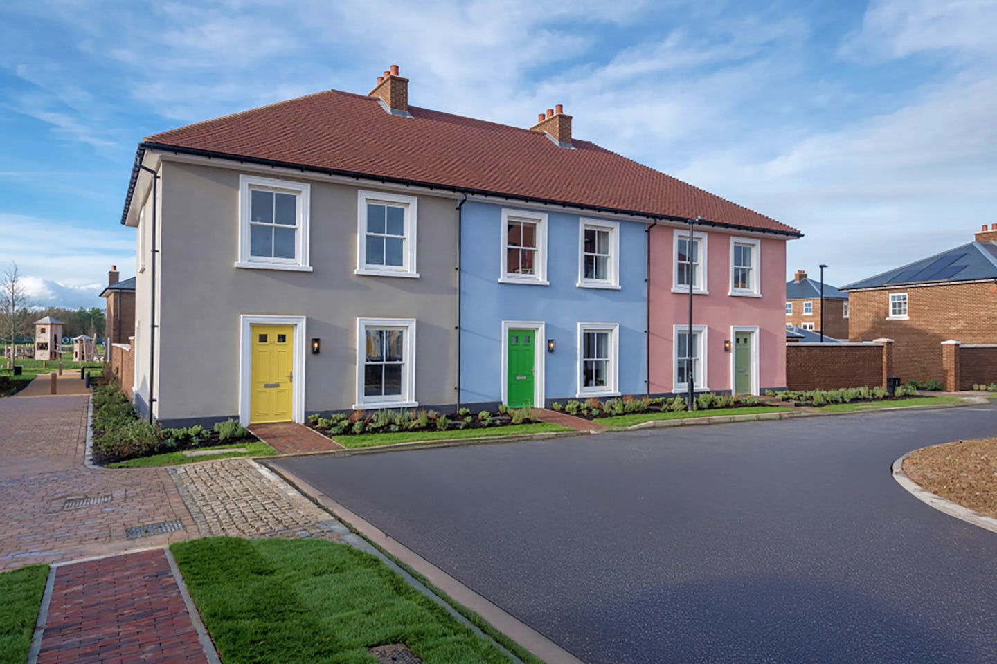 A row of newly built terraced houses with pastel‑coloured fronts and a quiet residential road in front.
