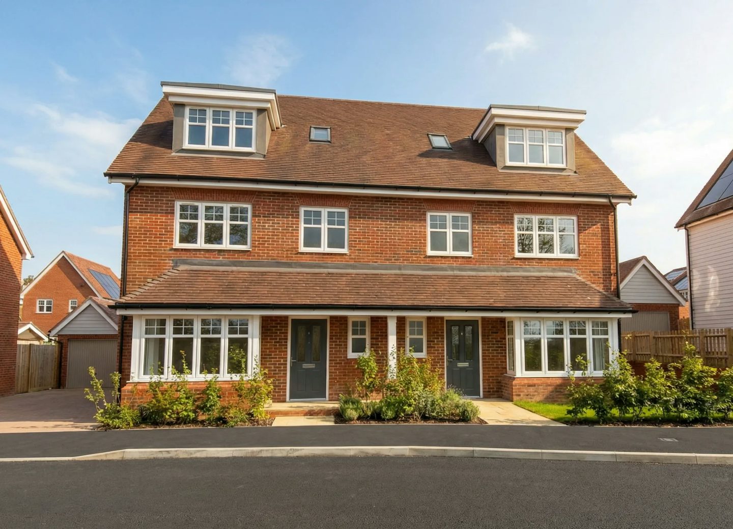 Front view of a modern red‑brick semi‑detached house with two front doors and dormer windows.