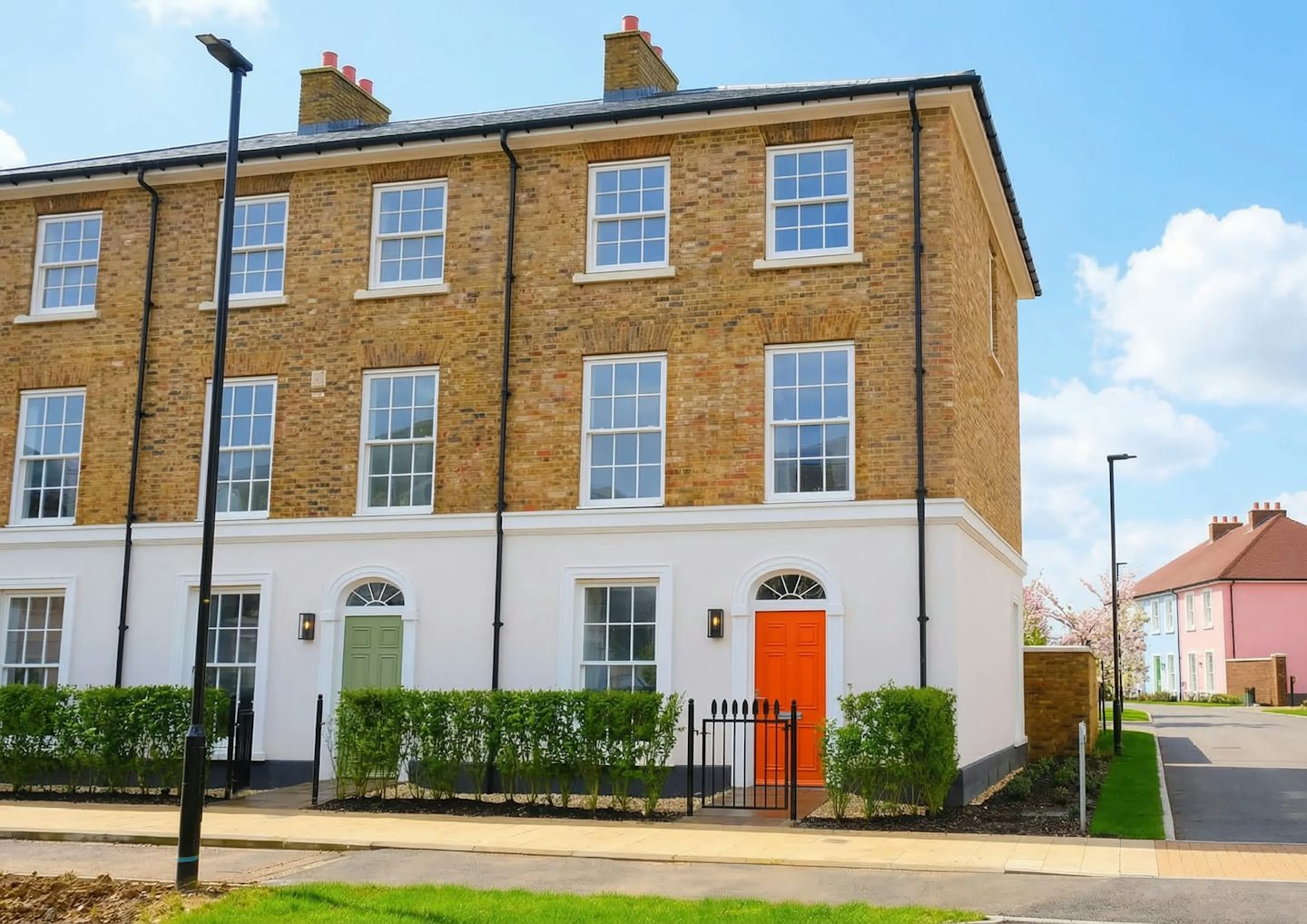 Corner view of a three‑storey brick townhouse with white ground floor detailing and a coloured front door.
