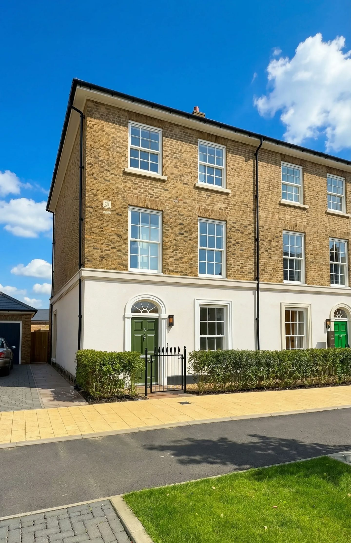 Front view of a three‑storey brick townhouse with a green front door and small front hedge.