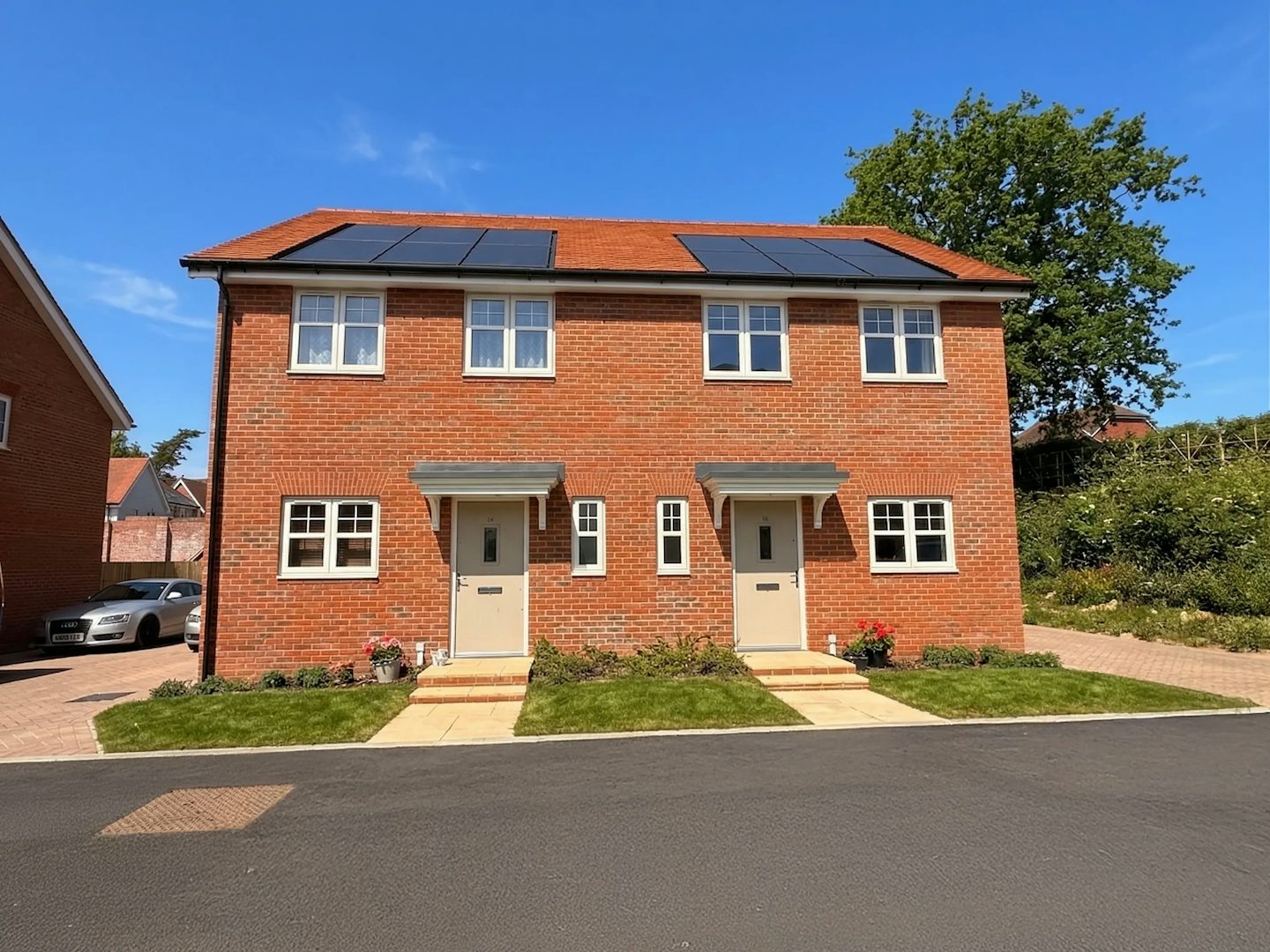 Front view of a red‑brick semi‑detached house with solar panels on the roof and two front doors.