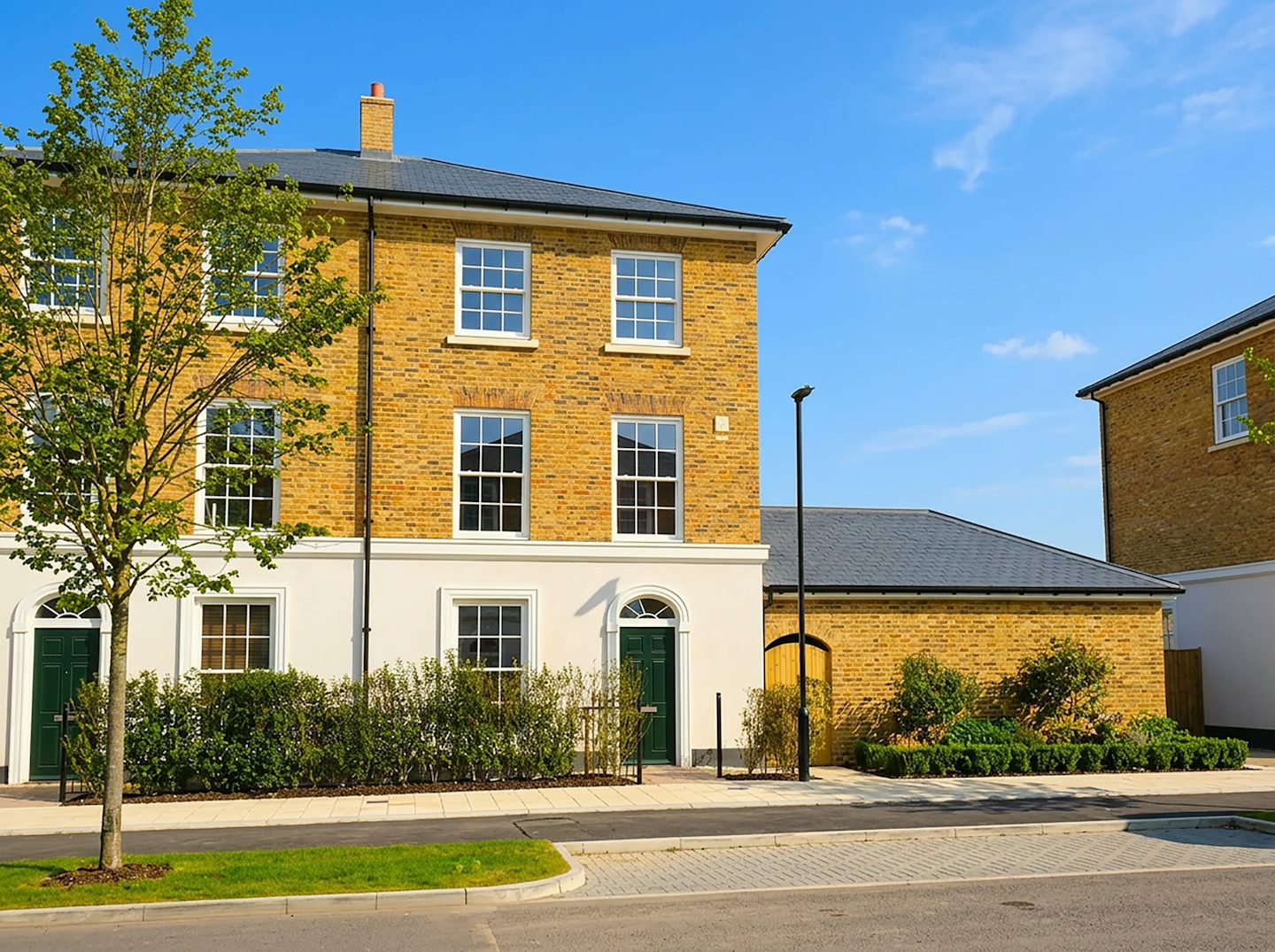 Front view of a three-storey brick house with white detailing, green front door, and landscaped planting along the pavement.