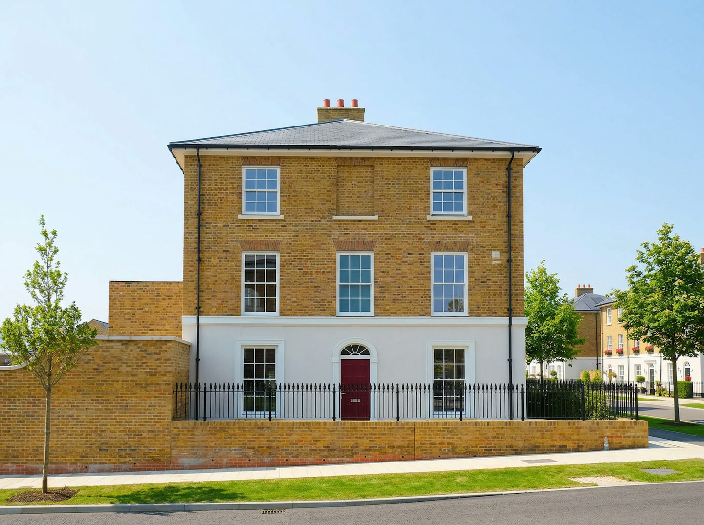 Front view of a three-storey brick house with white ground-floor detailing, red front door, and low brick boundary wall.