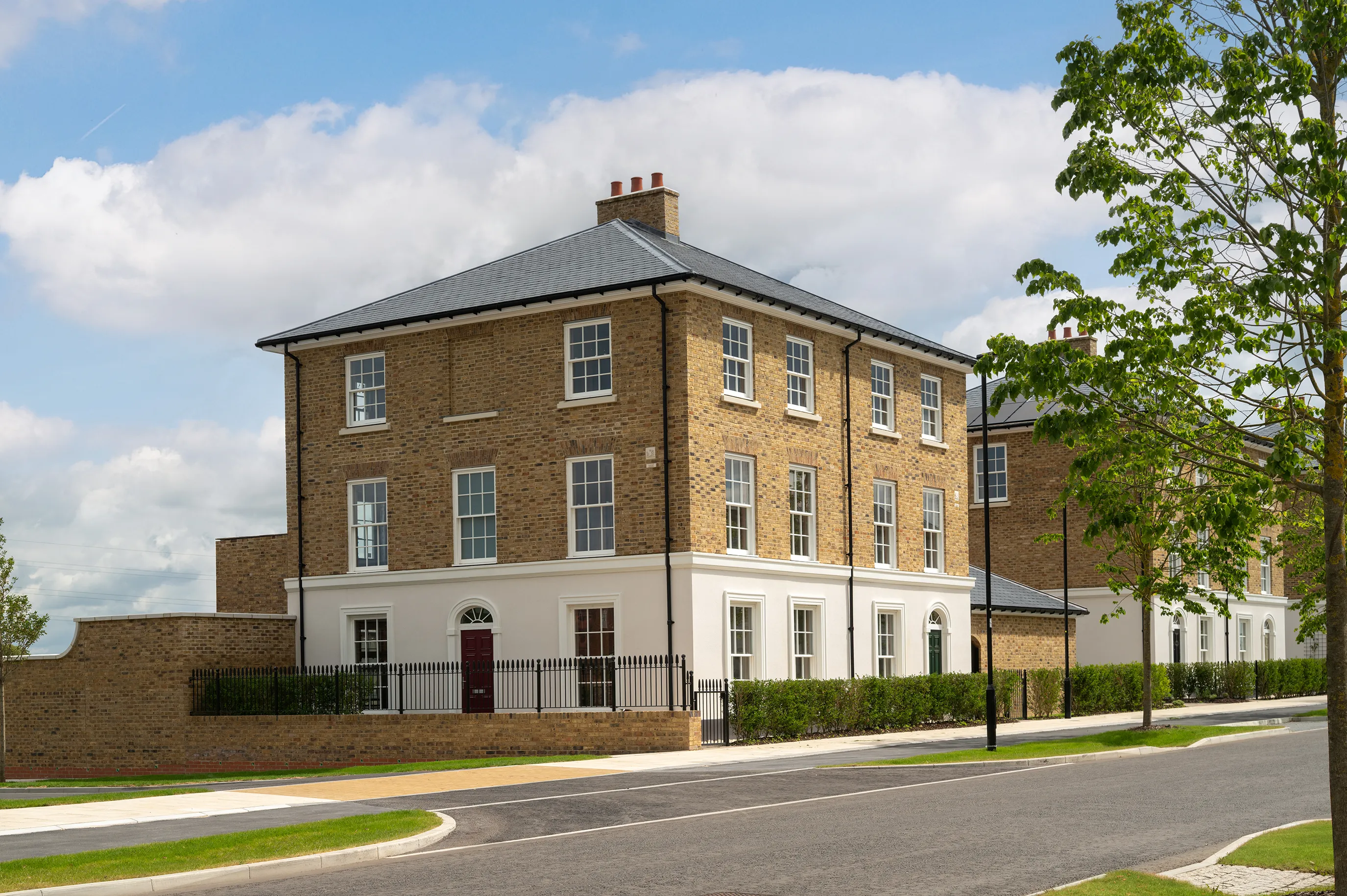 Large three-storey brick townhouse on a corner plot with white ground floor, black railings, and a quiet road in front