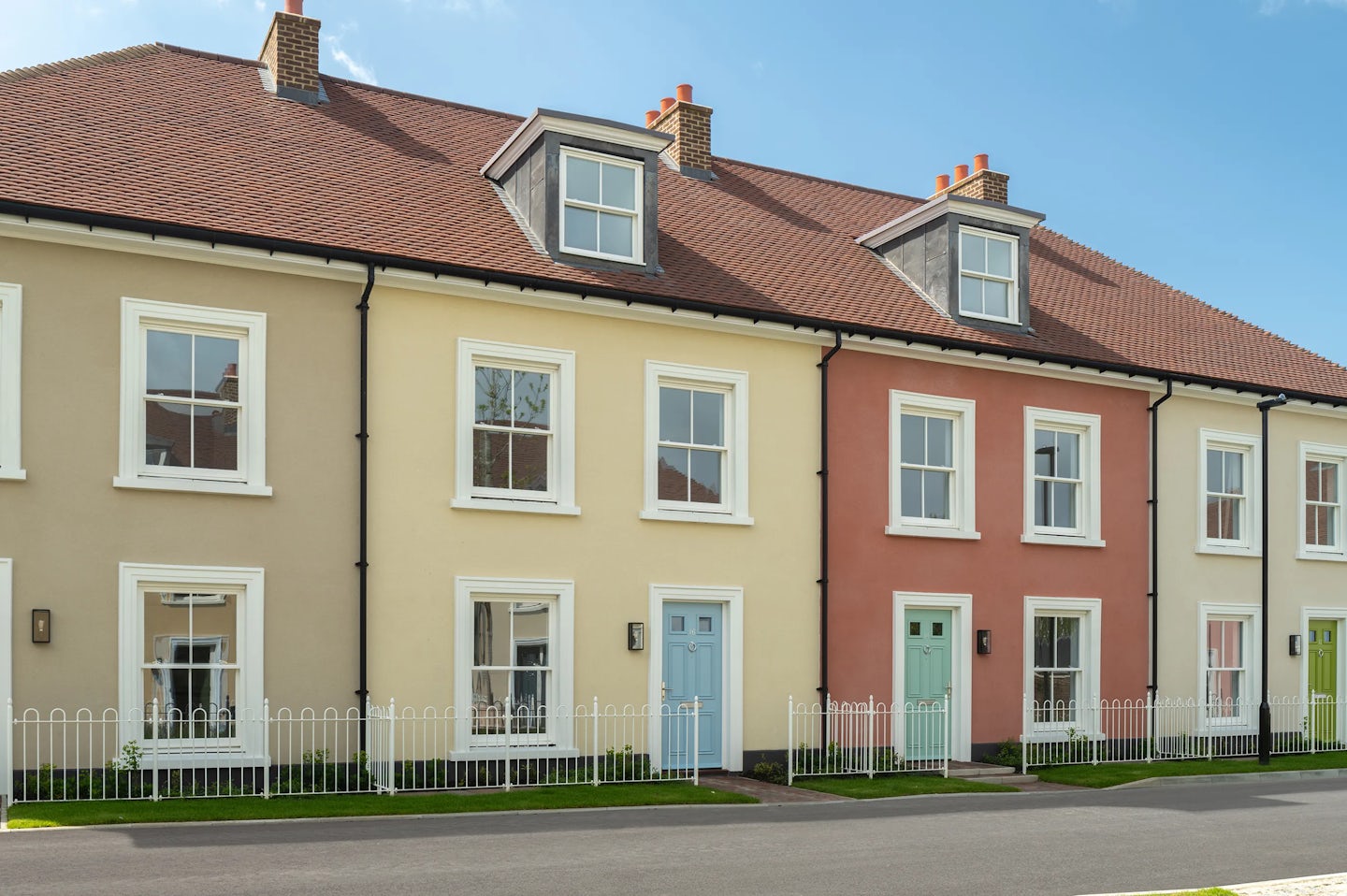 Row of terraced houses with cream and red walls, white windows, and pastel coloured front doors behind a low white fence