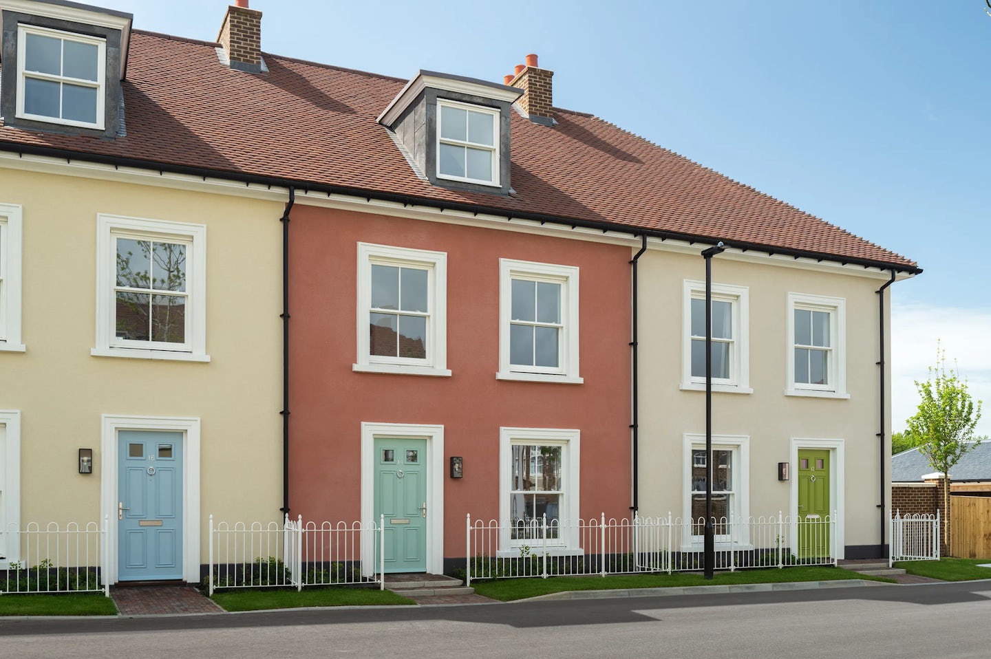 Terraced houses with cream and red walls, white windows, and coloured front doors along a residential street
