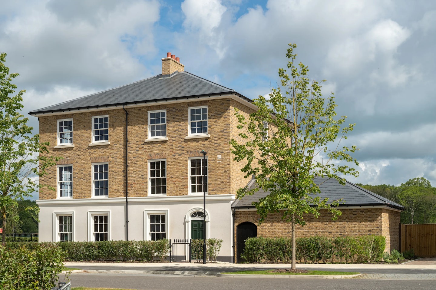 Large three-storey brick townhouse on a corner plot with trees and a garage, beside a residential street