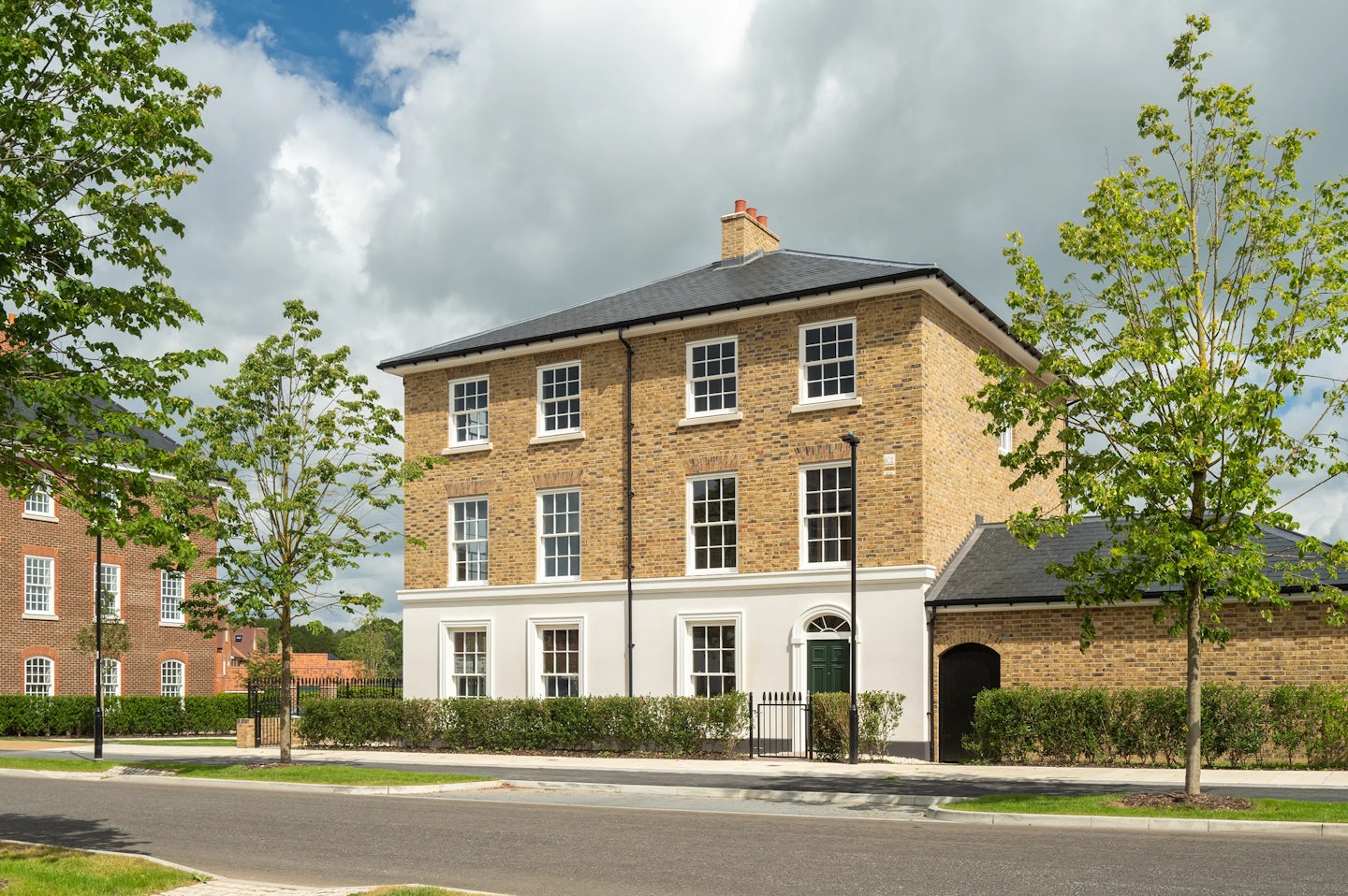 Large three-storey brick townhouse with white ground floor, trees and hedges in front, and a quiet road