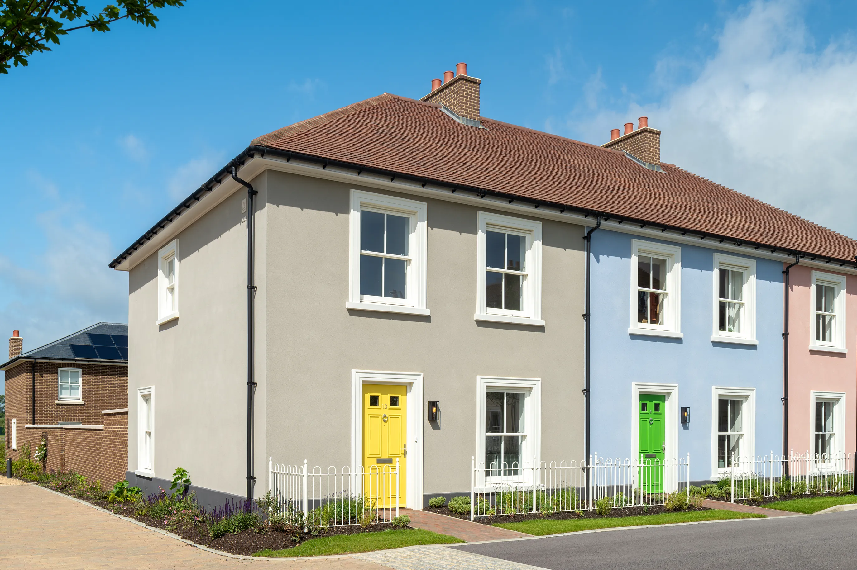 End of terrace houses with cream and blue walls, bright coloured front doors, and a small fenced garden along the pavement
