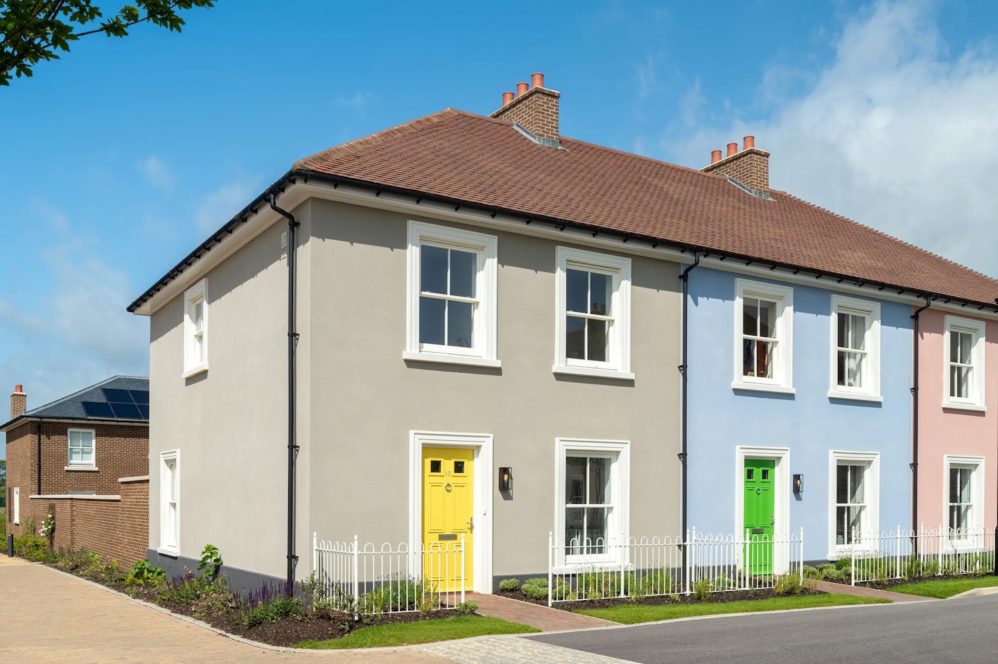 End of terrace houses with cream and blue walls, bright coloured front doors, and a small fenced garden along the pavement