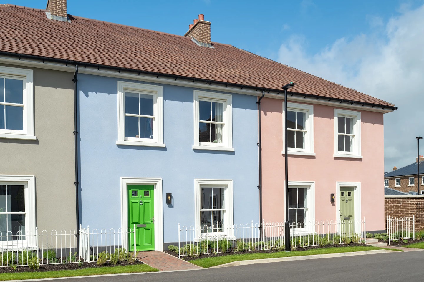 Row of terraced houses with blue and pink walls, white windows, and coloured front doors behind a low white fence