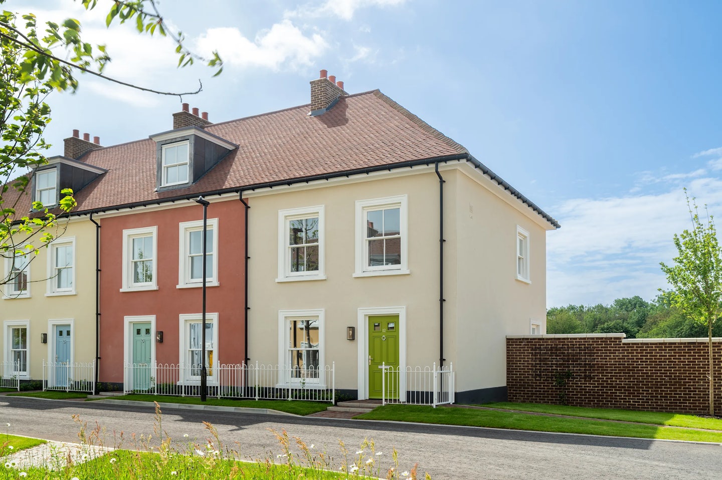 End of terrace houses with cream and red walls, a green front door, and a low brick wall to the side