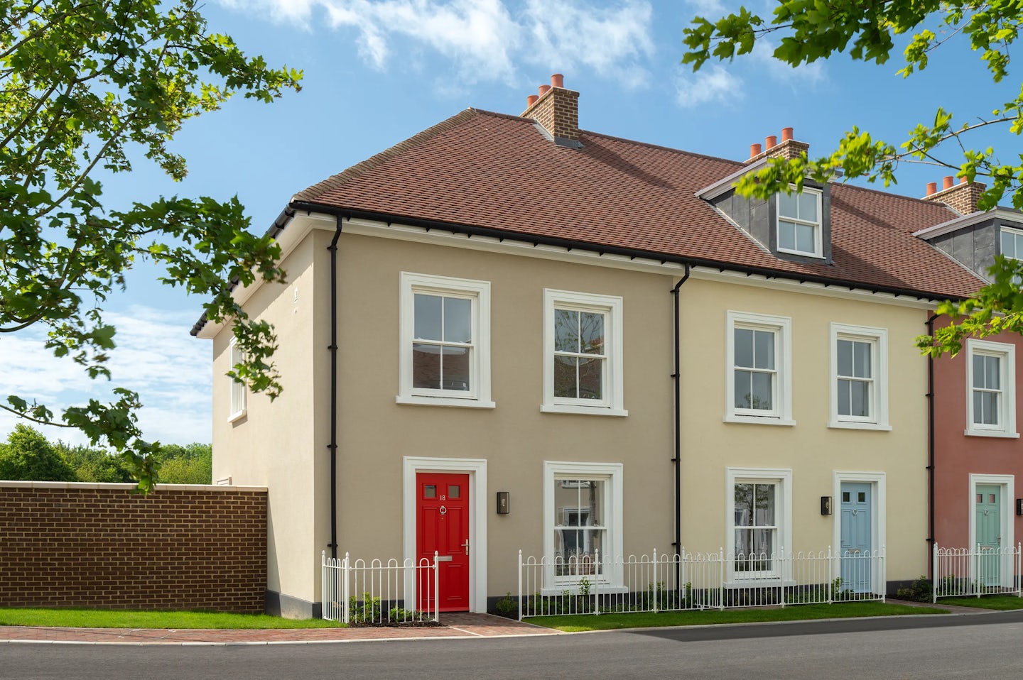 End of terrace houses with cream walls, white windows, and a red front door along a residential street