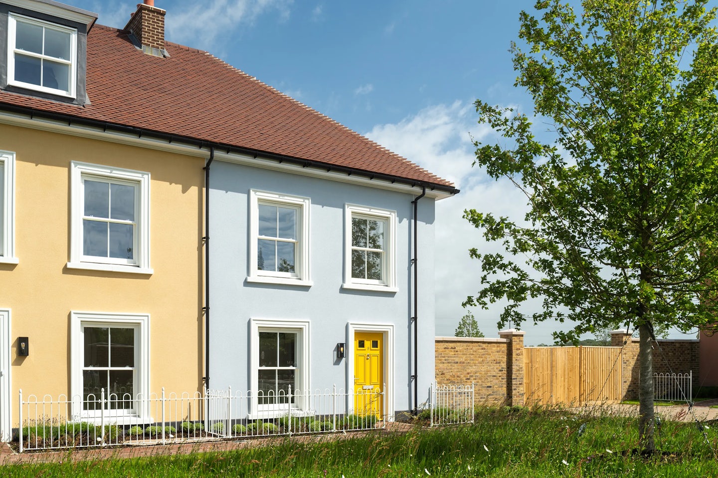 End of terrace houses with cream and light blue walls, a yellow front door, and a small garden with a tree in front