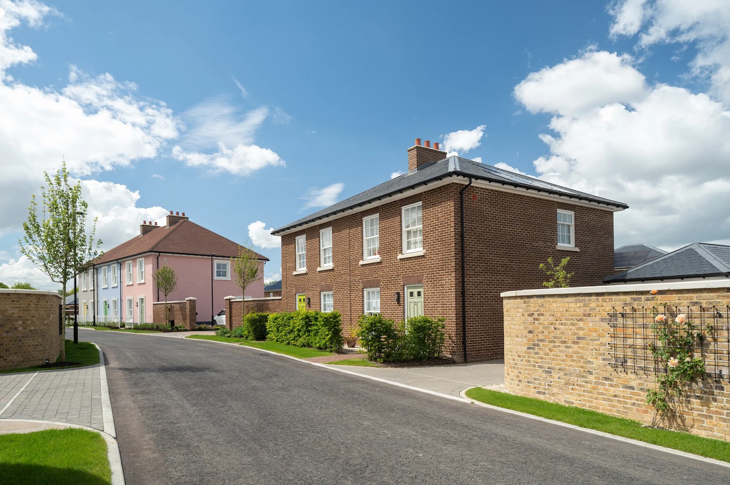 Large two-storey brick houses with white ground floor, trees and hedges along a quiet road