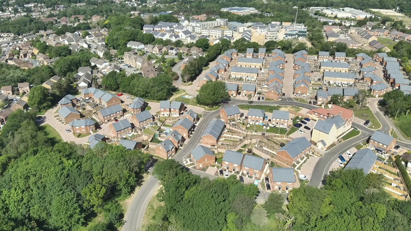 Wide aerial view of a completed housing scheme with uniform rooflines, private gardens and landscaped edges connecting to surrounding green space.