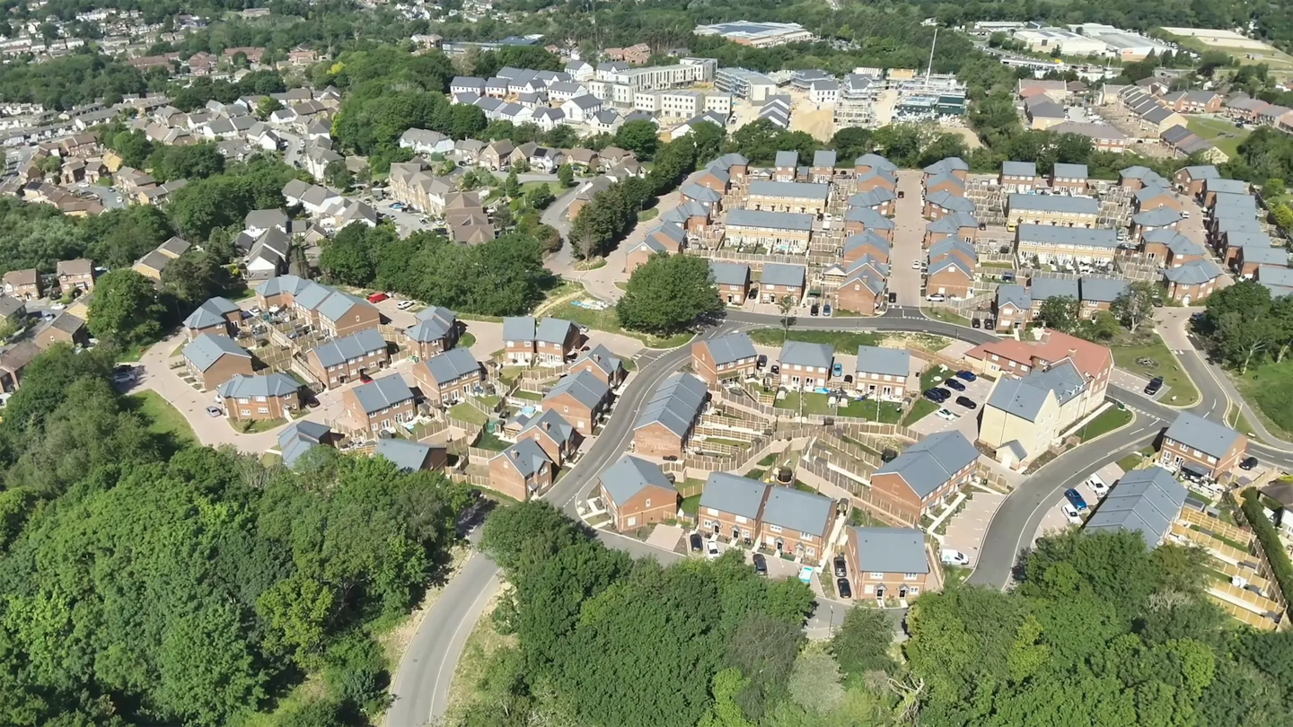 Wide aerial view of a completed housing scheme with uniform rooflines, private gardens and landscaped edges connecting to surrounding green space.