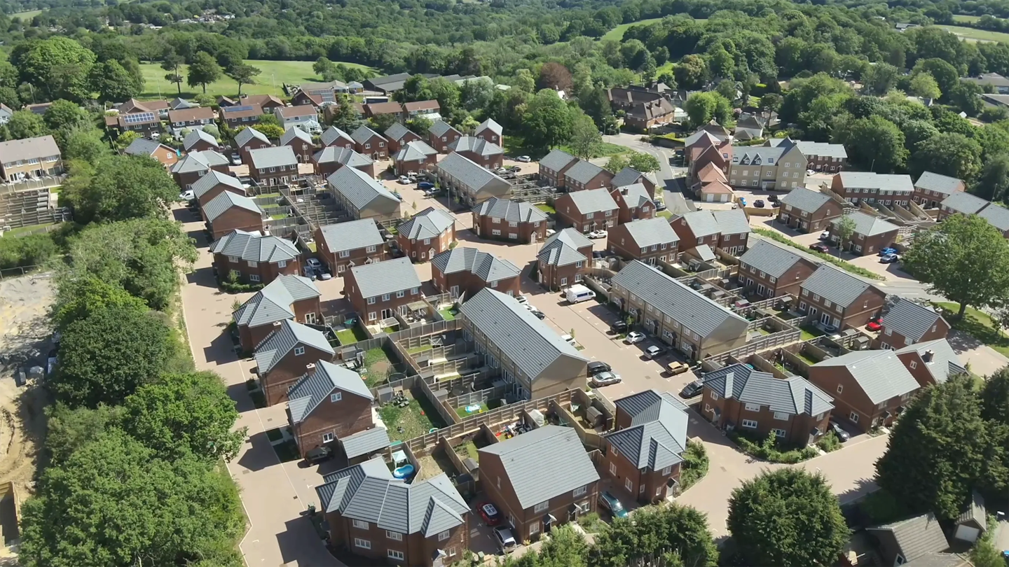 High-level aerial of a housing development within a wider townscape, showing nearby construction works and surrounding residential areas.