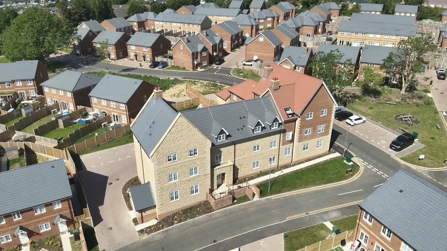 Street-level aerial view focused on a three-storey apartment building with a stone and brick façade, set within a new residential area.