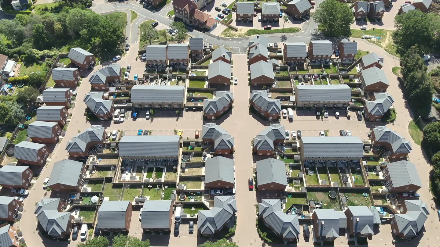 Top-down aerial view of a residential street layout with terraced and detached homes, private gardens and parked cars arranged around a central road.