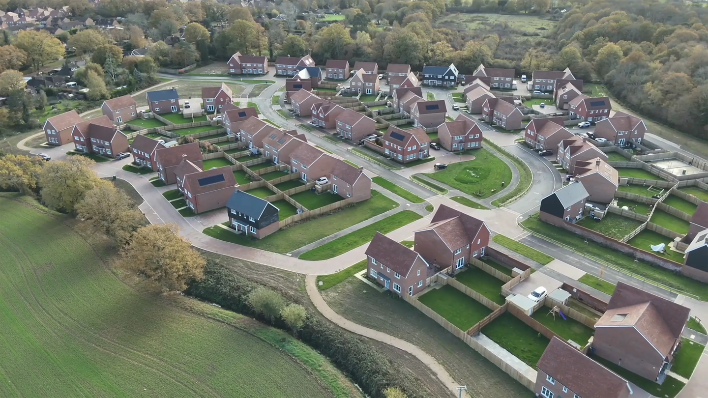 Aerial view of homes arranged along curving streets with footpaths and landscaped edges connecting to surrounding countryside.