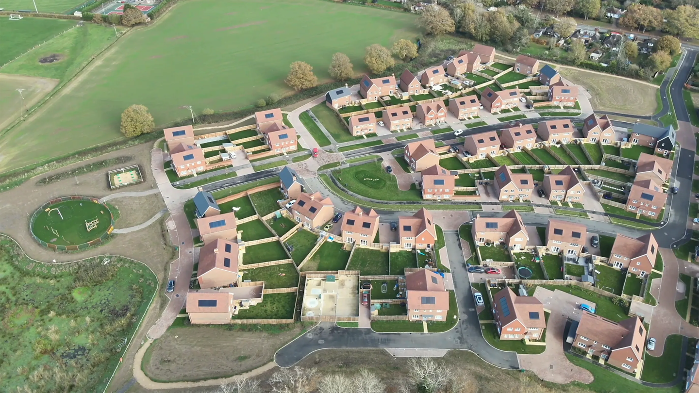 Top-down aerial view showing homes arranged around a central green space and play area, with enclosed gardens and footpaths linking streets.
