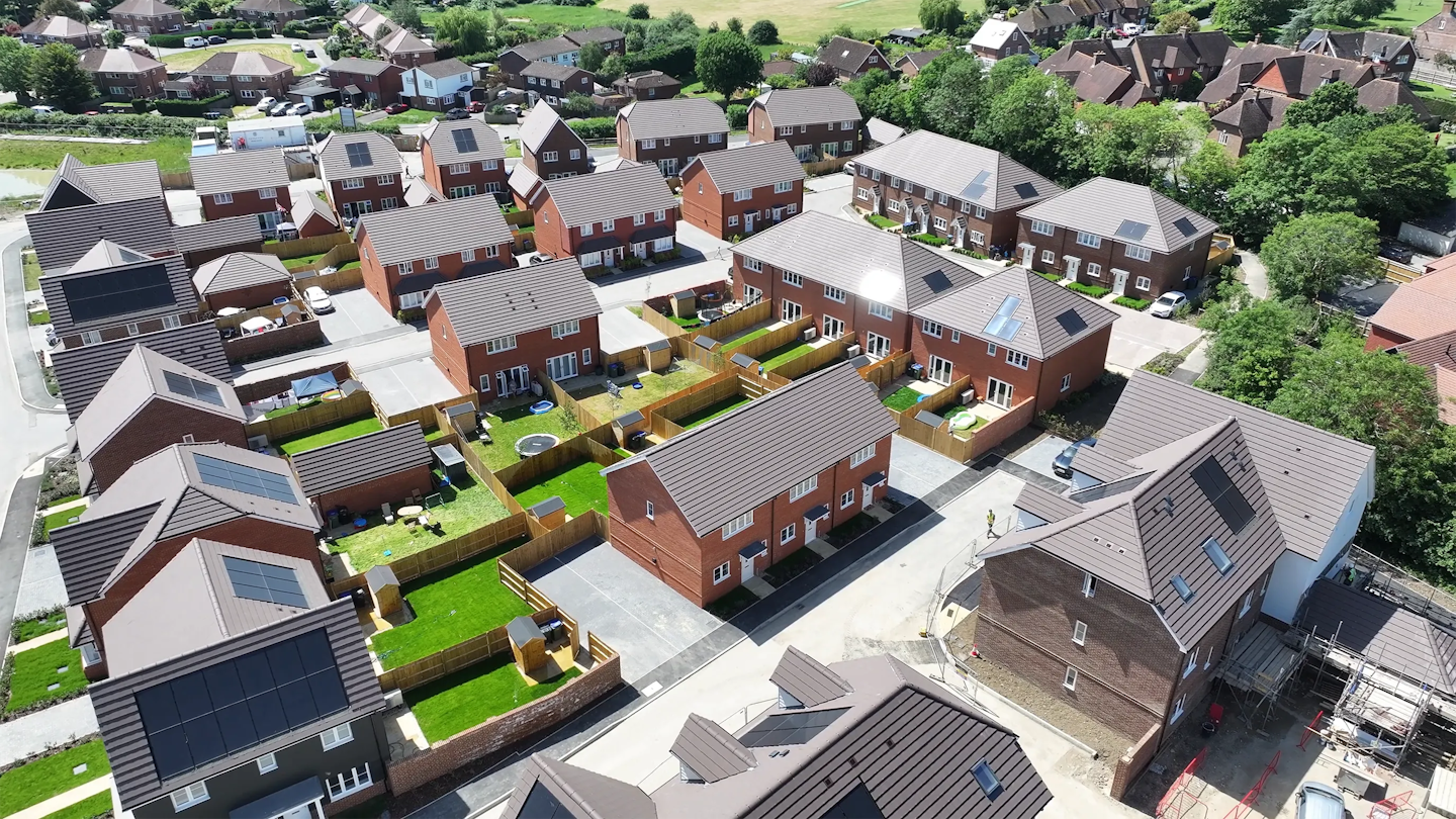 Closer aerial view of homes with private rear gardens, fences, and cars parked along a residential street within the development.