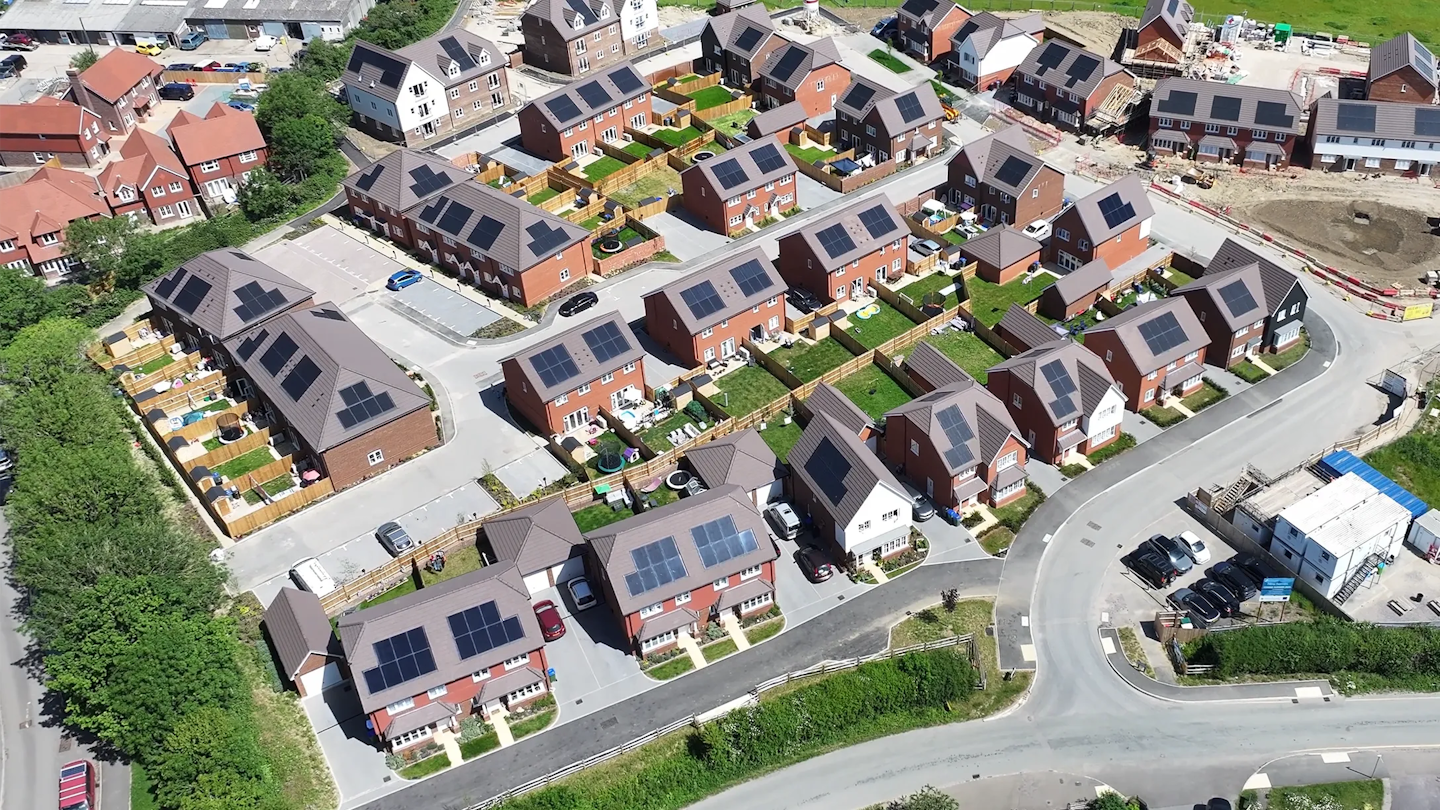 Oblique aerial view of the wider development with a mix of house types, roads, parking areas and adjacent construction works.