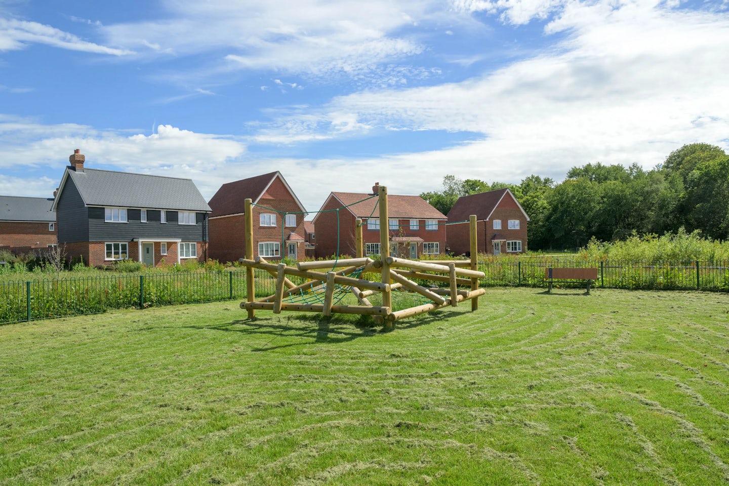 Small play area with wooden climbing frame on grass, with houses behind.