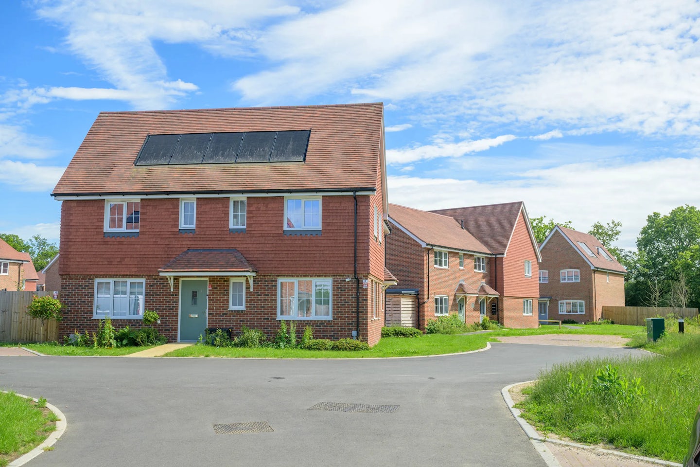 Corner view of red brick houses with pitched roofs, solar panels and shared road space.