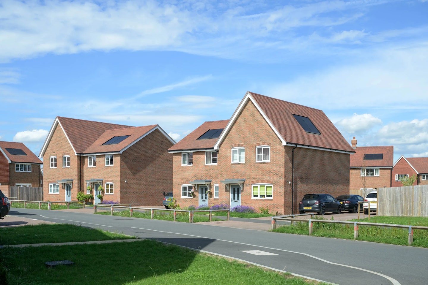 Row of red brick houses with solar panels, small front gardens and on-street parking.