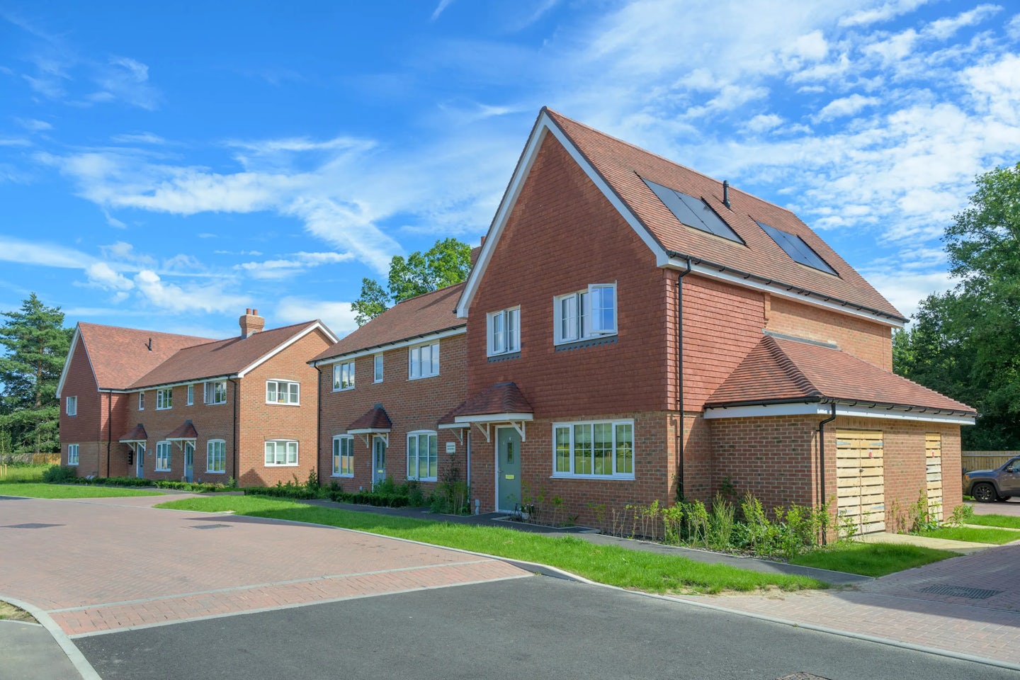 New homes with brick and tile facades, solar panels on roofs, and a landscaped street with paths