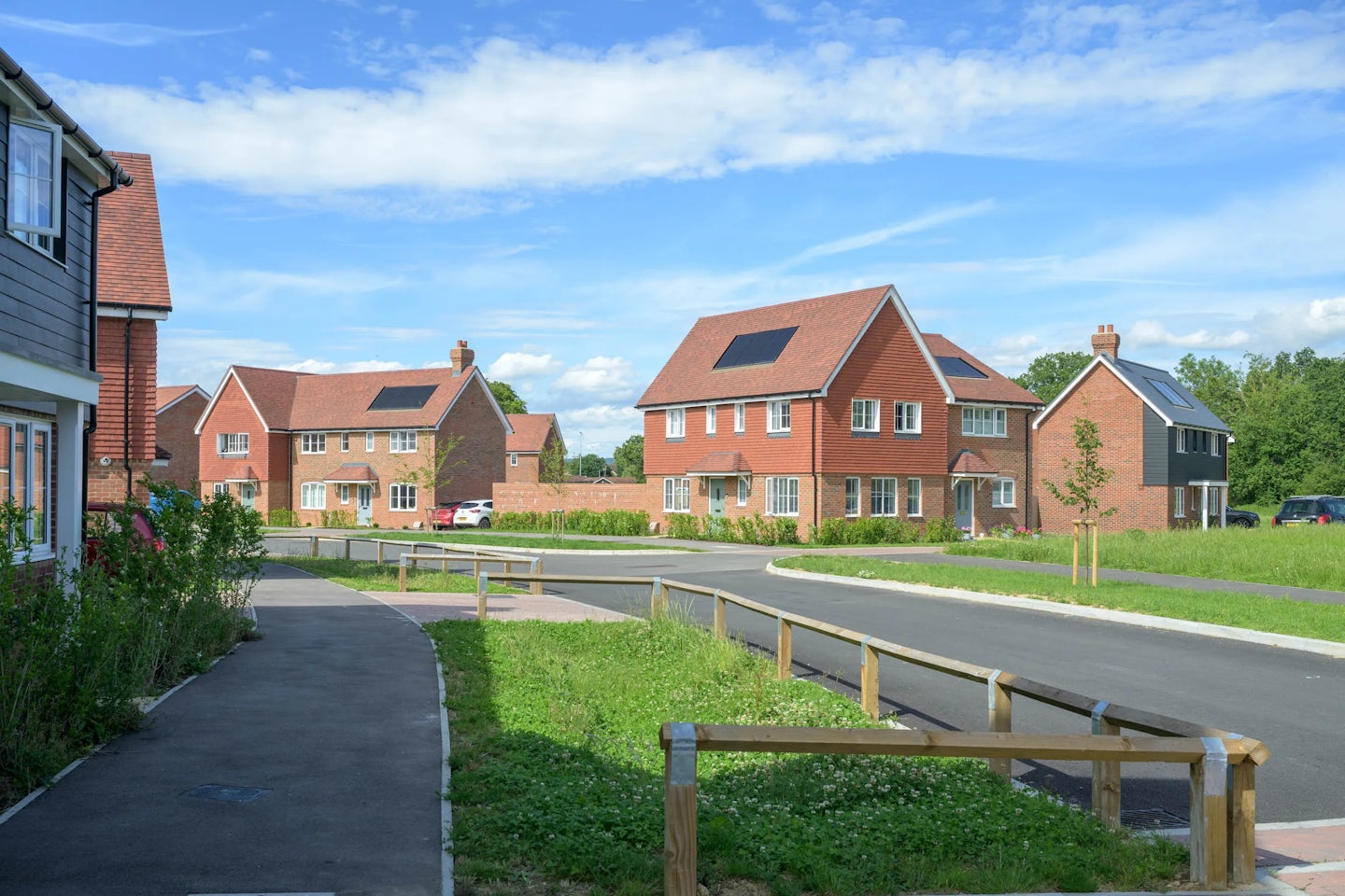 Residential street in a new housing development with detached houses, greenery and parked cars