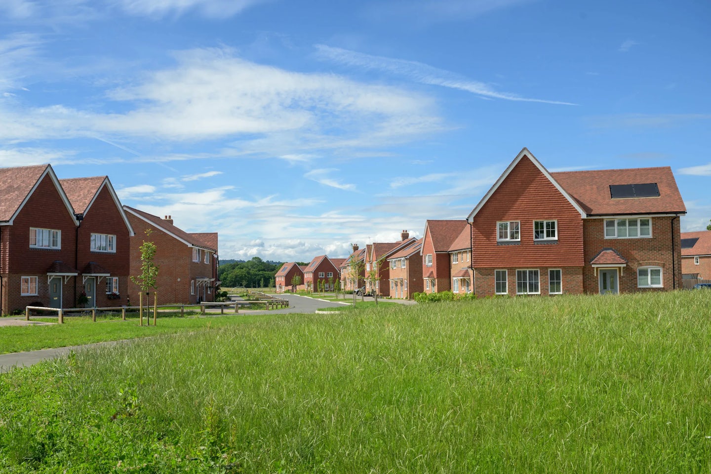New housing development with red brick homes beside open green space and a curved road