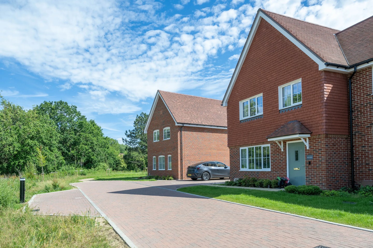 Red brick houses with pitched roofs and driveways beside green space and planting.