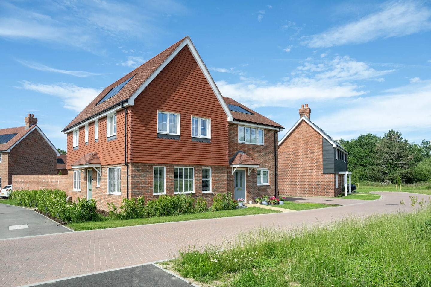 Pair of new semi-detached houses with brick and tile cladding, front doors and planted borders