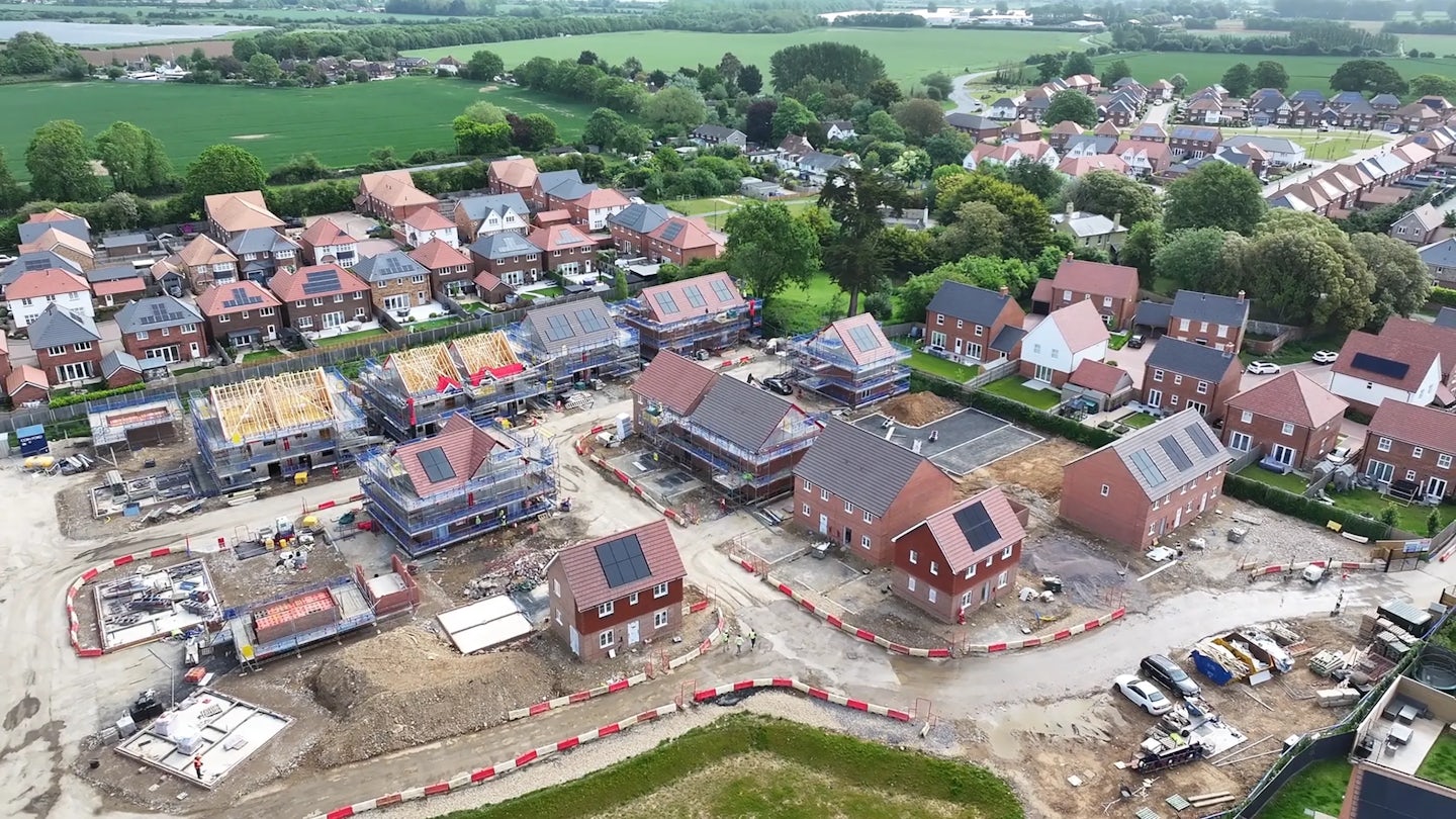 Drone view of partially completed houses with roof structures in place and surrounding residential area