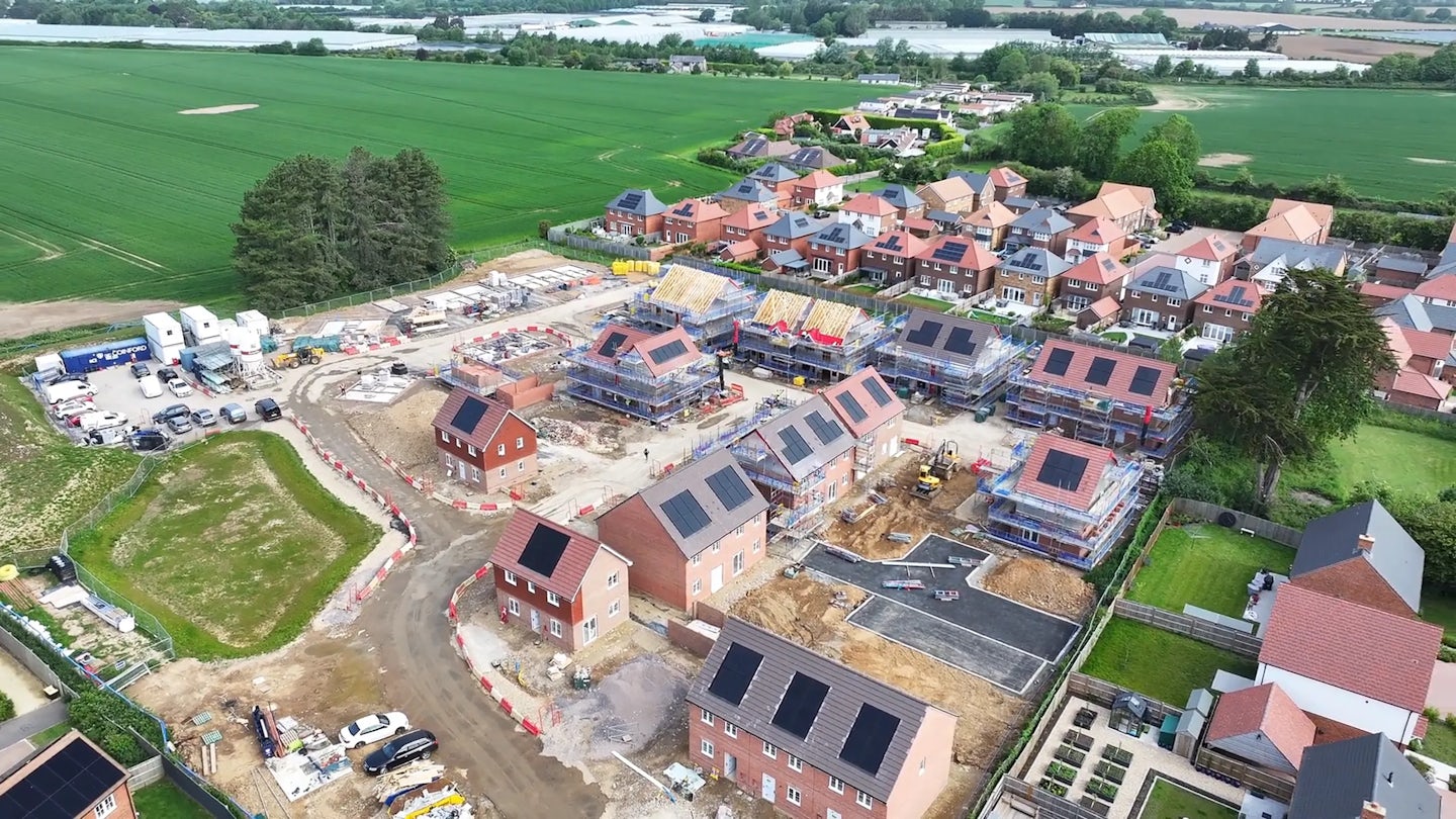 Wide aerial view of new homes being built next to an existing neighbourhood and open farmland