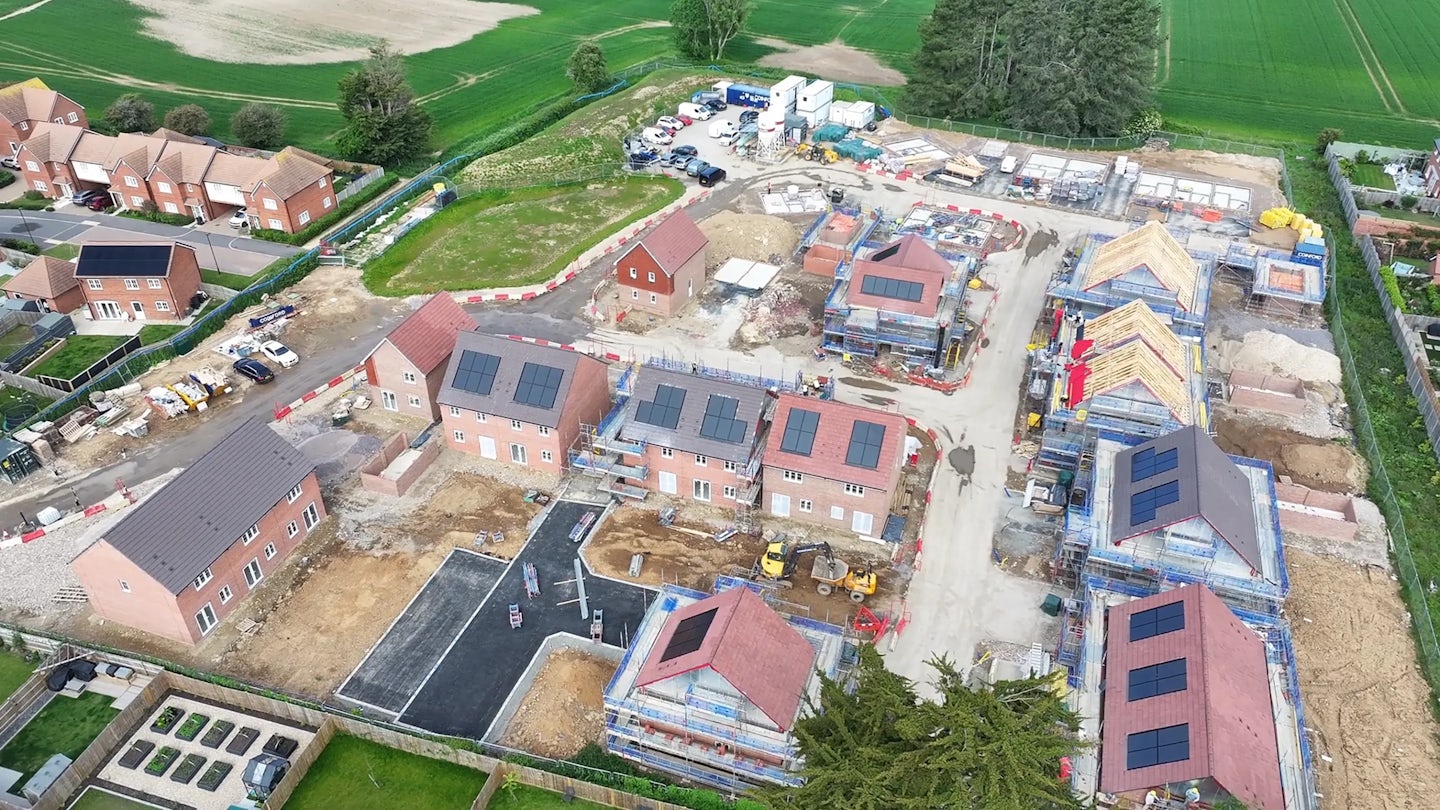 Aerial view of a housing development under construction with brick homes, scaffolding and site cabins