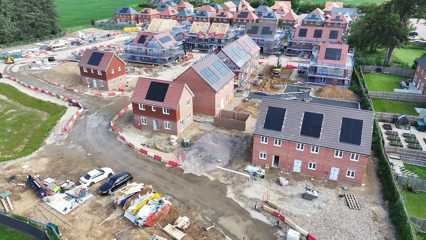 Housing site in progress with scaffolding, groundwork and machinery, set near established homes and fields
